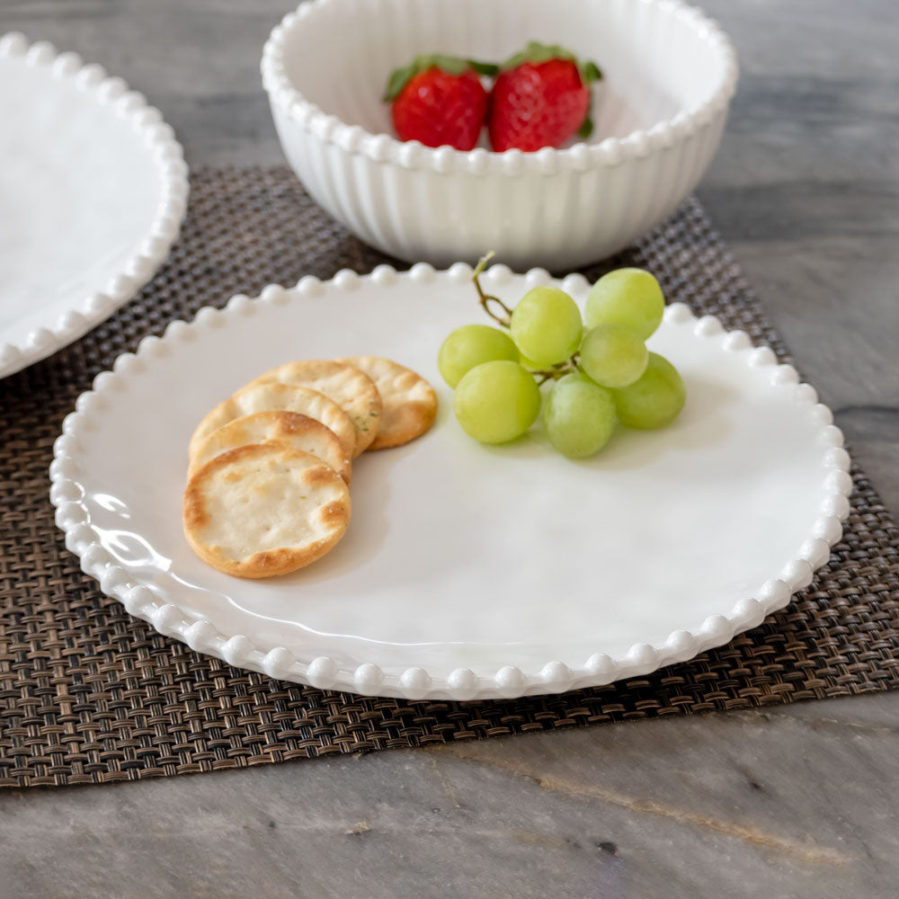 Cream colored, 8-inch round melamine salad plate with salad, on granite countertop next to salad bowl and dinner plate with fruits and crackers