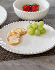 Cream colored, 8-inch round melamine salad plate with salad, on granite countertop next to salad bowl and dinner plate with fruits and crackers