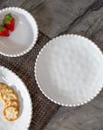 Cream colored, 8-inch round melamine salad plate with salad, on granite countertop next to salad bowl and dinner plate with fruits and crackers
