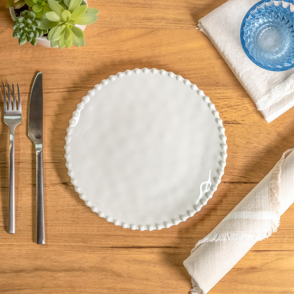 Cream colored, 8-inch round melamine salad plate, top view, with silverware, napkin, and blue tumbler on a wooden table