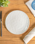 Cream colored, 8-inch round melamine salad plate, top view, with silverware, napkin, and blue tumbler on a wooden table