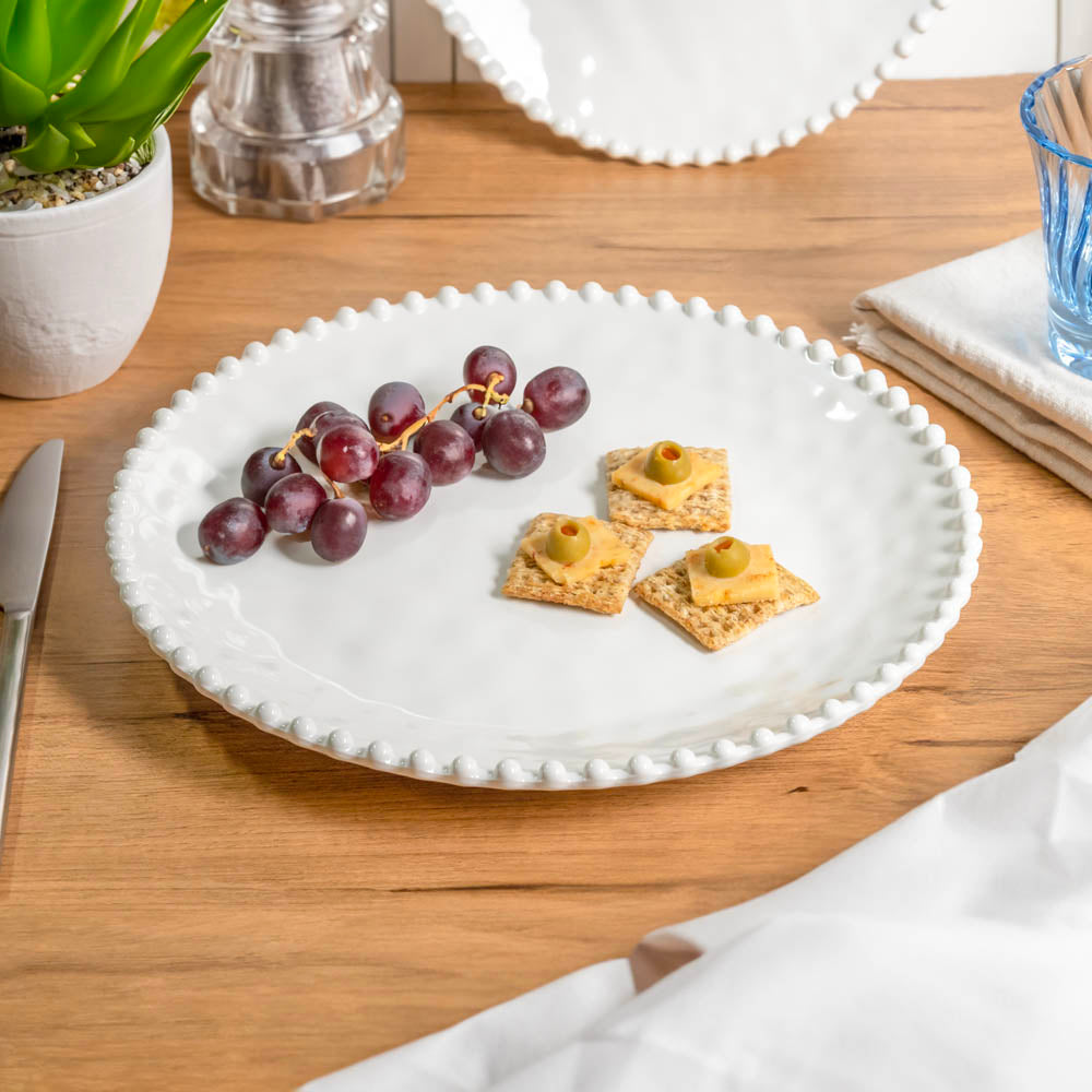 Cream colored, 11-inch melamine dinner plate set with beaded rim on a wooden table with acrylic tumbler, salad bowl, and napkin