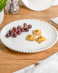 Cream colored, 11-inch melamine dinner plate set with beaded rim on a wooden table with acrylic tumbler, salad bowl, and napkin