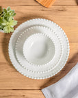 Cream colored, stacked melamine dinnerware set including 11-inch melamine dinner plate, salad bowl, and salad plate on a wooden table