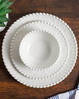 Cream colored, stacked melamine dinnerware set including 11-inch melamine dinner plate, salad bowl, and salad plate on a wooden table