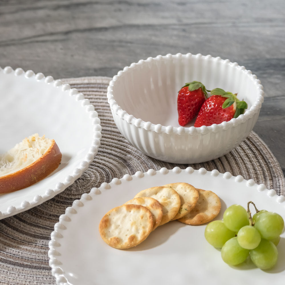 Cream colored, 6-inch round melamine salad bowl with salad, stacked with dinner plate and salad plate on granite countertop, with strawberries, crackers, and green grapes.