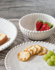 Cream colored, 6-inch round melamine salad bowl with salad, stacked with dinner plate and salad plate on granite countertop, with strawberries, crackers, and green grapes.