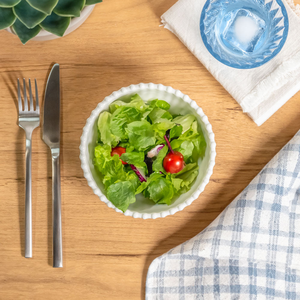 Cream colored, 6-inch round melamine salad bowl with salad on a wooden table, next to a blue acrylic tumbler, silverware, and napkin