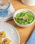 Cream colored, 6-inch round melamine salad bowl with salad on a wooden table, next to a blue acrylic tumbler, silverware, and napkin