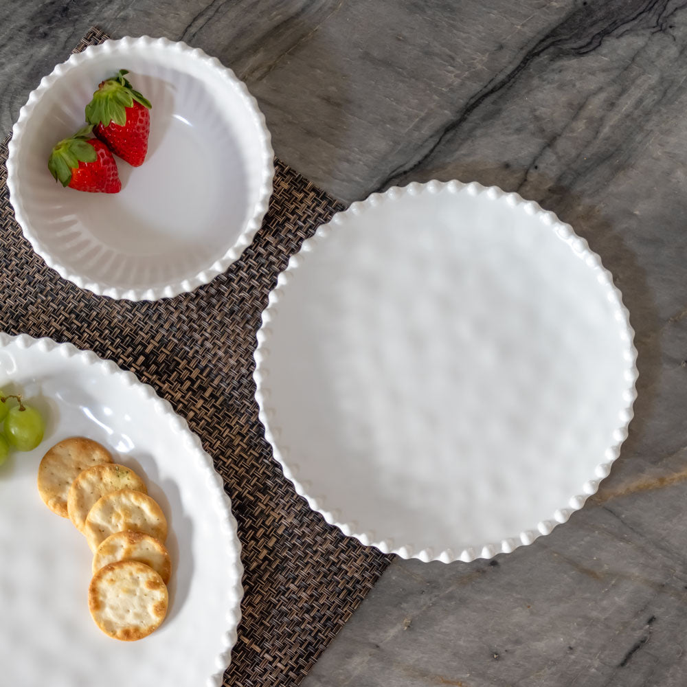 Cream colored, 8-inch round melamine salad plate with salad, on granite countertop next to salad bowl and dinner plate with fruits and crackers