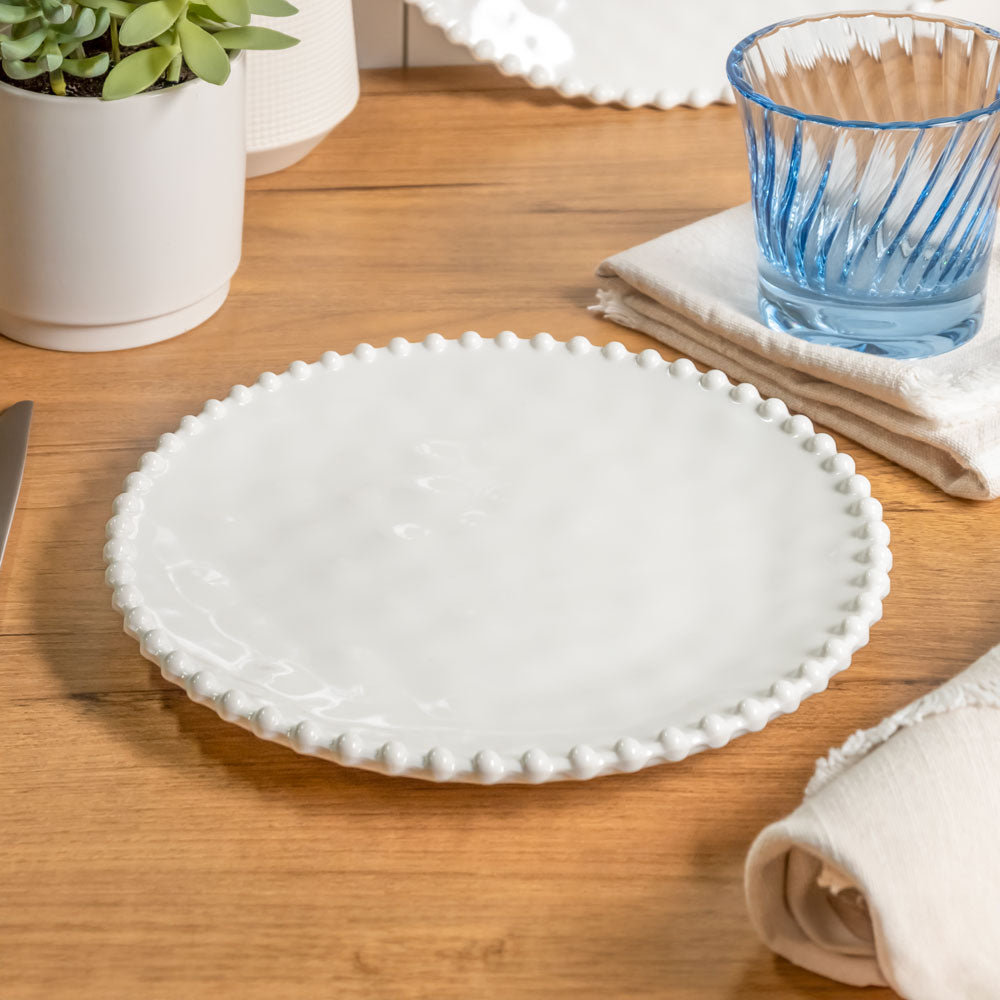 Cream colored, 8-inch round melamine salad plate, top view, with silverware, napkin, and blue tumbler on a wooden table