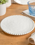 Cream colored, 8-inch round melamine salad plate, top view, with silverware, napkin, and blue tumbler on a wooden table