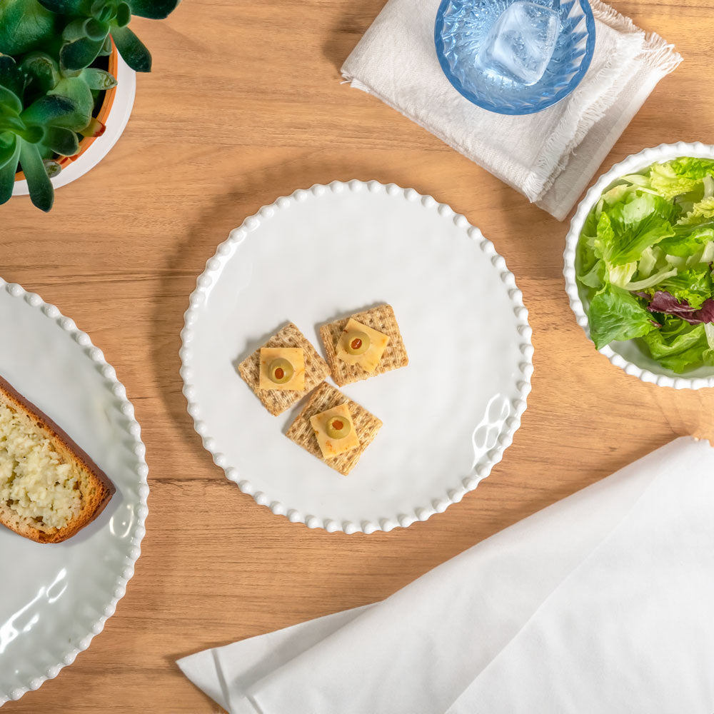 Cream colored, 8-inch round melamine salad plate, top view, with silverware, napkin, and blue tumbler on a wooden table