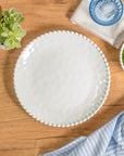 Cream colored, 11-inch melamine dinner plate set with beaded rim on a wooden table with acrylic tumbler, salad bowl, and napkin