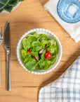 Cream colored, 6-inch round melamine salad bowl with salad on a wooden table, next to a blue acrylic tumbler, silverware, and napkin