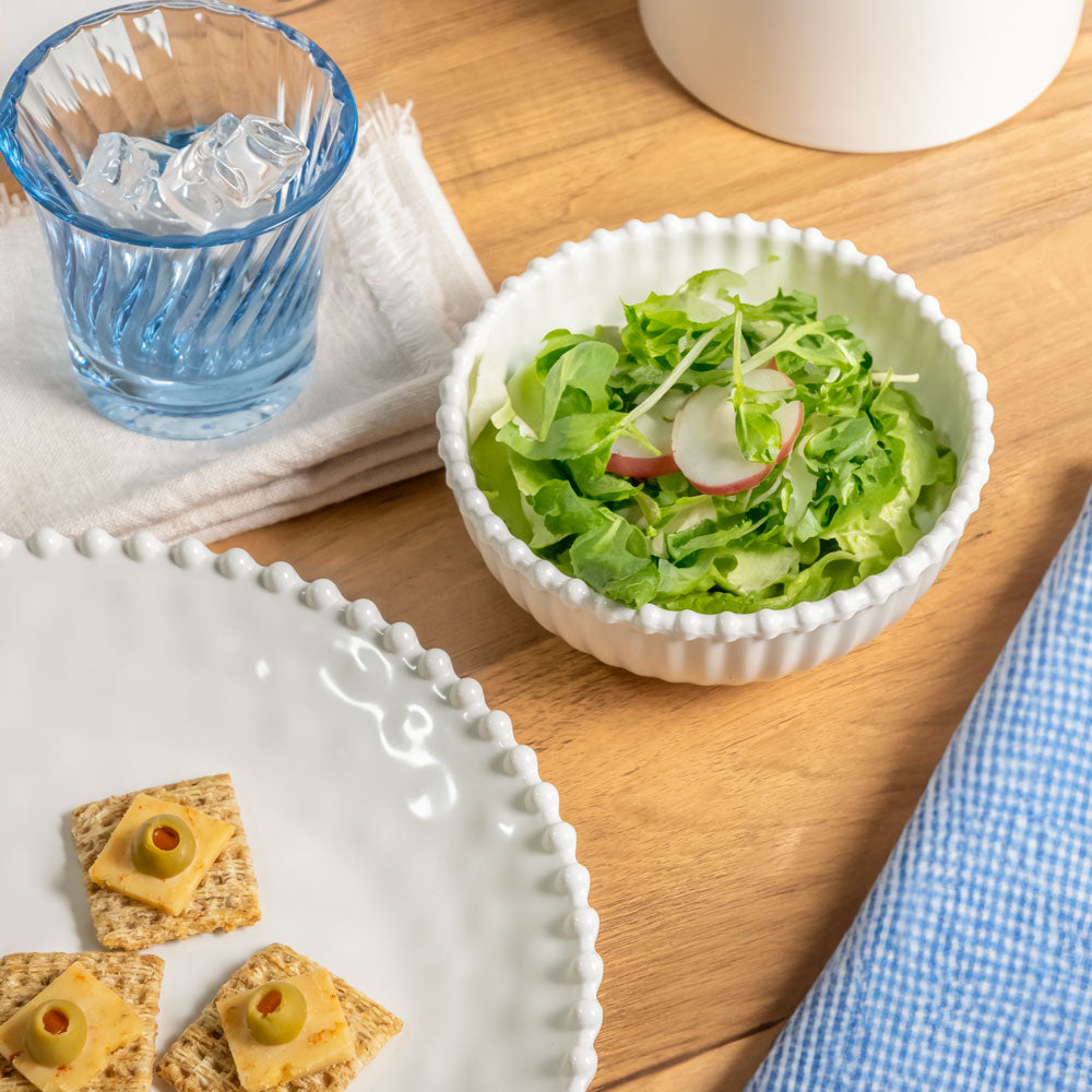 Cream colored, 6-inch round melamine salad bowl with salad on a wooden table, next to a blue acrylic tumbler, silverware, and napkin